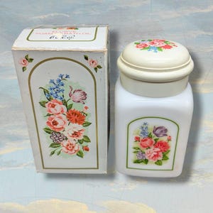 May include: A vintage white cosmetic jar and matching box. Both feature floral designs in pink, red, blue, and purple. The jar has a rounded lid and a rectangular body. The box is rectangular with an arched floral design.