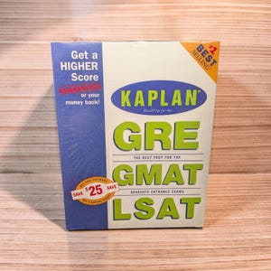 May include: A Kaplan GRE prep book with the text "Get a HIGHER Score" and "GUARANTEED or your money back!". The book also says "GRE THE BEST PREP FOR THE GMAT LSAT". The cover is white, blue, and green.