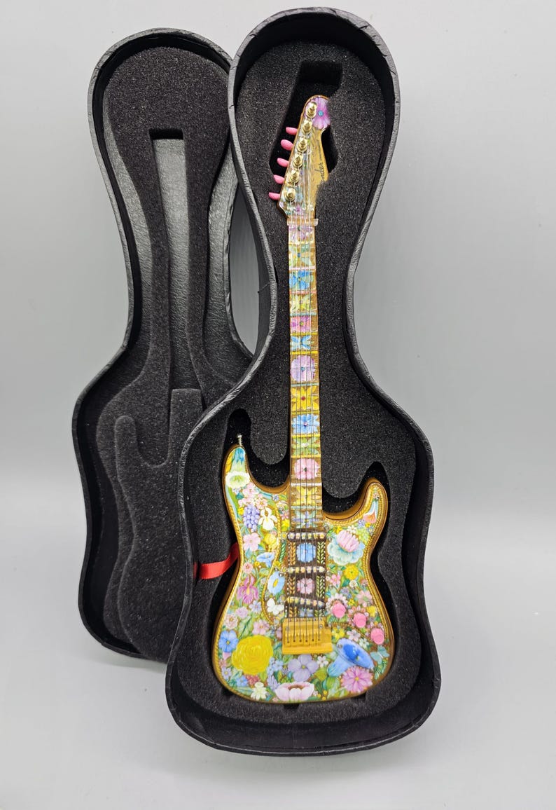 May include: A miniature electric guitar with a floral design in shades of pink, yellow, blue, and green. The guitar is in a black hard case.