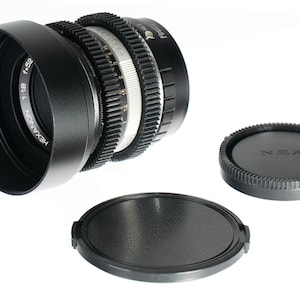 May include: A black Hexanon f/1.8 52mm camera lens with a lens hood and two lens caps. The lens has a silver and black focus ring and is set against a white background.