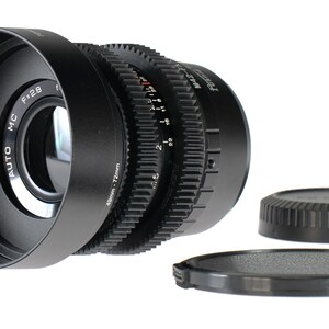 May include: A black camera lens with a lens hood, and two lens caps. The lens has a series of ridged rings for focus and aperture control. The lens is marked with "AUTO MC F:2.8" and "68mm - 72mm".