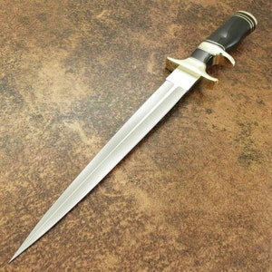 May include: A silver dagger with a black and gold handle. The blade is long and sharp, and the handle is decorated with a black and gold pattern.