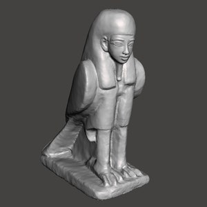 Puede incluir: Una escultura de piedra gris de un pájaro con cabeza humana con un rostro detallado y un cuerpo emplumado. La escultura está de pie sobre una base rectangular.
