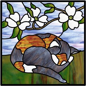 Op de afbeelding: Een gebrandschilderd raam met daarop een driekleurige kat die in slaap is gerold op een bed van groen gras met witte kornoelje bloesems op de achtergrond.