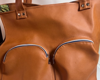 May include: A brown leather tote bag with two zippered pockets on the front. The bag has a white and blue trim around the zipper openings.