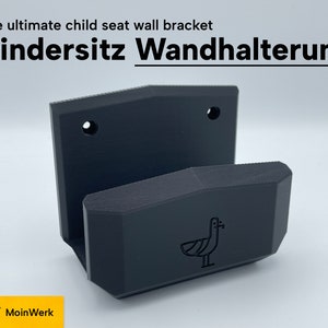 Könnte beinhalten: Schwarze Wandhalterung aus Kunststoff für einen Kindersitz. Die Halterung hat ein schlichtes Design mit abgerundeter Kante und einem kleinen Vogel-Logo. Der Text "Kindersitz Wandhalterung" ist auf dem Bild zu sehen.