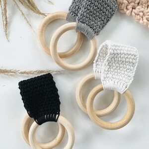 Puede incluir: Tres anillos de madera con bucles de tela de crochet en gris, blanco y negro. Los anillos est&aacute;n apilados uno encima del otro.