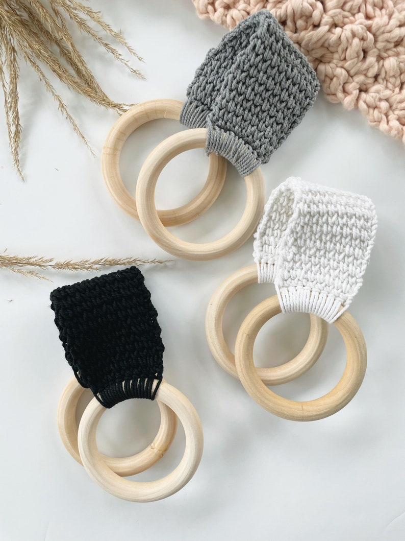Puede incluir: Tres anillos de madera con bucles de tela de crochet en gris, blanco y negro. Los anillos est&aacute;n apilados uno encima del otro.