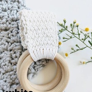 Puede incluir: Anillo de crochet blanco con un anillo de madera adjunto. El anillo de crochet tiene un patr&oacute;n texturizado. El anillo de madera est&aacute; hecho de dos anillos, uno dentro del otro. Los anillos est&aacute;n sobre una superficie blanca.