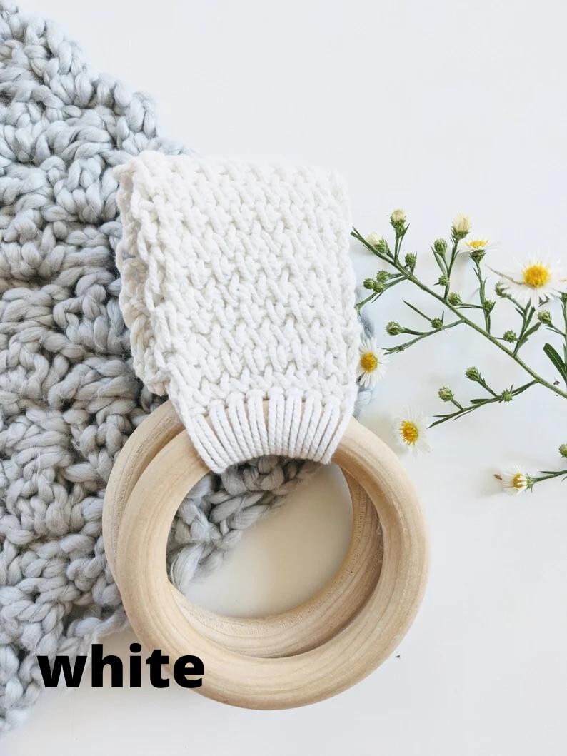 Puede incluir: Anillo de crochet blanco con un anillo de madera adjunto. El anillo de crochet tiene un patr&oacute;n texturizado. El anillo de madera est&aacute; hecho de dos anillos, uno dentro del otro. Los anillos est&aacute;n sobre una superficie blanca.