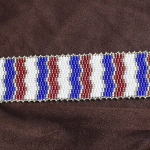 May include: A beaded bracelet with a wavy pattern in red, white, and blue colors. The bracelet has a silver clasp.