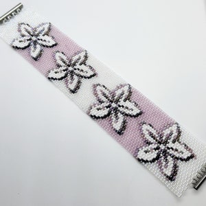 May include: A white and pink beaded bracelet with a repeating pattern of white flowers. The bracelet has silver clasps on each end.