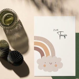 May include: A white card with a rainbow and a cloud with a smiley face. The text "ZUR Taufe" is written in black at the top of the card.