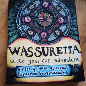 Puede incluir: Una portada de libro con un diseño de brújula colorido y el título "WAS SURETTA write your own adventure". El texto "written by Tamsin Balcanquall Illustrated by sabracadabra" también está en la portada.