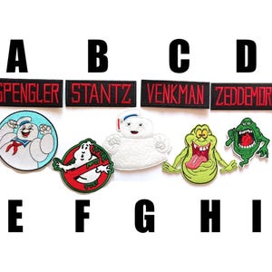 May include: Nine embroidered patches featuring characters and names from the Ghostbusters film. The patches are black with red and white lettering. The characters include Slimer, Stay Puft Marshmallow Man, and the Ghostbusters logo.