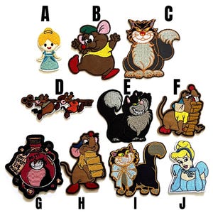 Può includere: Una collezione di toppe ricamate raffiguranti personaggi dei cartoni animati. Le toppe includono una ragazza bionda in un vestito blu, un topo marrone, un gatto nero con un sorriso malizioso e altri personaggi.