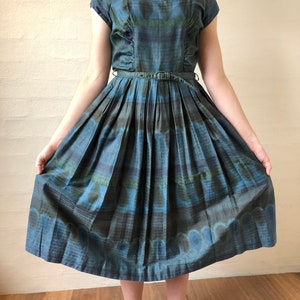 May include: A blue and green patterned dress with a fitted bodice and a full skirt. The dress has a scoop neckline and short sleeves. The skirt is pleated and has a belt at the waist.