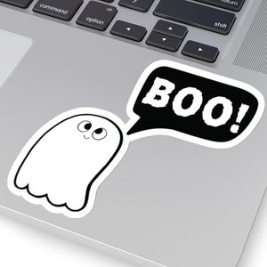 May include: A white ghost with a friendly face and big eyes is saying "BOO!" in a black speech bubble. The ghost is on a silver laptop.