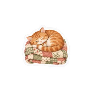 May include: A sleeping orange tabby cat with a small gold bell collar curled up on a folded patchwork quilt. The quilt features a repeating pattern of muted pink, cream, and sage green squares with delicate floral and leaf motifs throughout.