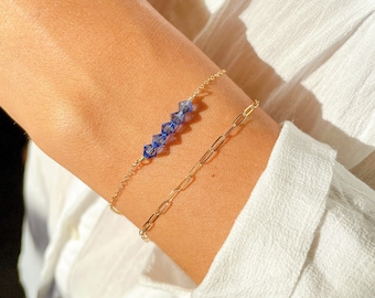 May include: A gold chain bracelet with a delicate chain and a row of blue crystal beads.