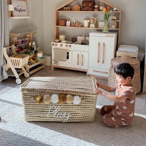 May include: A child's playroom with a woven storage chest labelled "Play" and a wooden play kitchen. The room features a shopping cart, shelves, and a lion-shaped wall decoration. The overall aesthetic is light and airy.