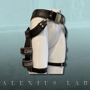 May include: A black leather and brown suede harness with silver-tone hardware. The harness features a wide belt, adjustable straps, and multiple loops. The text "ALEXIUS LAB" is at the bottom of the image.