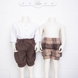 May include: Two mannequins wearing brown shorts. One pair of shorts is a solid brown colour, and the other pair is a plaid pattern with brown and beige squares.
