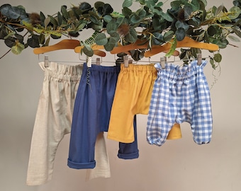 May include: Four pairs of children's pants hanging on a clothesline. The pants are made of different fabrics and colors, including beige, blue, yellow, and blue and white gingham.