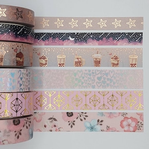 May include: A set of eight pink and gold washi tapes with various patterns, including stars, moons, hearts, geometric shapes, and floral designs.