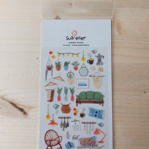 Pu&ograve; includere: Un foglio di adesivi trasparenti con illustrazioni di oggetti per la decorazione della casa, tra cui un divano, una lampada, un calendario, una pianta in vaso, un cesto, uno specchio, una caffettiera, un libro e un gatto. Gli adesivi sono etichettati "Sua elier, suatelier stickers, no.1075: home sweet home".