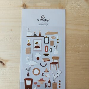 Pu&ograve; includere: Un foglio di adesivi con illustrazioni di vari oggetti di arredamento in stile minimalista. Gli adesivi sono in tonalit&agrave; di marrone, beige e bianco. Il foglio &egrave; etichettato "Suatelier stickers no.33101 - objet".
