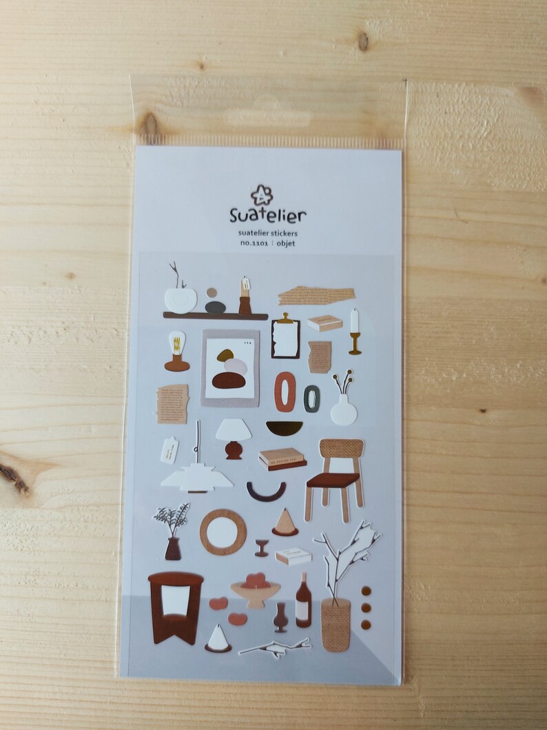 Pu&ograve; includere: Un foglio di adesivi con illustrazioni di vari oggetti di arredamento in stile minimalista. Gli adesivi sono in tonalit&agrave; di marrone, beige e bianco. Il foglio &egrave; etichettato "Suatelier stickers no.33101 - objet".