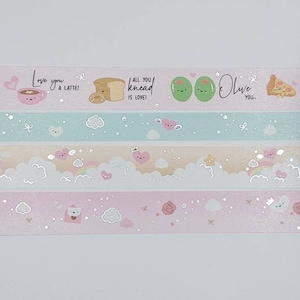 May include: Four rolls of washi tape with different designs. The first roll has a pink background with a heart, a cup of coffee, and the text "Love you a latte!" The second roll has a light blue background with clouds, stars, and hearts. The third roll has a light peach background with clouds, stars, and rainbows. The fourth roll has a light pink background with clouds, stars, and roses.