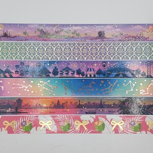 Puede incluir: Una colección de cintas washi decorativas con varios diseños. Las cintas muestran escenas como una puesta de sol, un circo, constelaciones y temas tropicales. Cada cinta tiene un patrón único con acentos dorados y colores vibrantes.