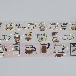 May include: Three rolls of washi tape with a coffee theme. The tape features illustrations of coffee cups, coffee makers, and coffee beans. The tape is decorated with gold stars.