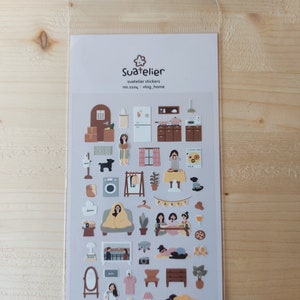Pu&ograve; includere: Un foglio di adesivi con illustrazioni di un interno di casa, tra cui mobili, piante e persone. Gli adesivi sono su uno sfondo grigio chiaro e hanno una gamma di colori marrone e beige. Il testo "Suatelier" e "no.1104. vlog_home" &egrave; stampato sul foglio.