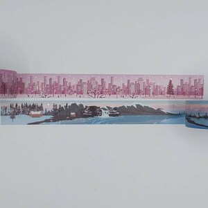 May include: A roll of washi tape featuring a winter city scene on a pink background and a snowy mountain scene on a blue background.