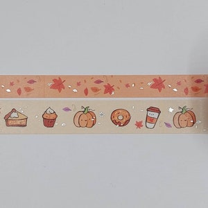 May include: Two rolls of washi tape with a fall theme. The top roll has a peach background with orange leaves and silver glitter. The bottom roll has a beige background with pumpkins, a pie, a cupcake, a donut, a coffee cup, and silver glitter.