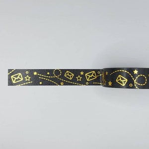 May include: Black washi tape with a gold foil design of stars, envelopes, and dotted lines.