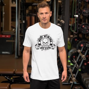 May include: White t-shirt with a black graphic featuring a skull, barbell, and the text "NO PAIN NO GAIN". The design is surrounded by a splatter effect. The shirt is made of a soft material.