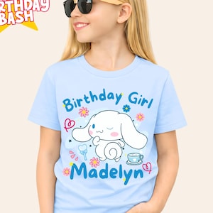May include: A pale blue t-shirt with the words "Birthday Girl" and "Madelyn" in blue script. The shirt features a cartoon character with long white ears and floral accents. The text "Jen Birthday Bash" is in a starburst.