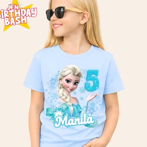 May include: A light blue t-shirt featuring a graphic of Elsa from Frozen, the number 5, and the name "Manila". The shirt also has a teal bow and snowflake accents. The words "Jen Birthday Bash" are in the upper left corner.