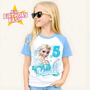 May include: A white and light blue raglan t-shirt featuring a graphic of Elsa from Frozen, the number 5, and the name "Manila". The shirt has the text "Jen Birthday Bash" in a starburst.