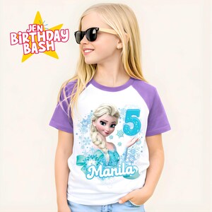 May include: White and purple raglan t-shirt featuring a cartoon image of Elsa from Frozen, with the number 5 in turquoise. The shirt also includes the name "Manila" and snowflake accents. The text "Jen Birthday Bash" is in a star-shaped graphic.