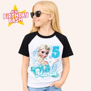 May include: A white and black raglan t-shirt featuring a cartoon image of Elsa from Frozen, the number 5, and the name "Manila" in blue. The shirt also has the text "Jen Birthday Bash" in a starburst graphic.