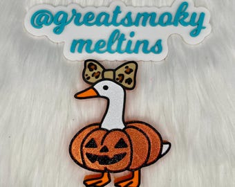 May include: A Halloween-themed decoration featuring a goose with a white head, orange beak, and a pumpkin body. The goose wears a leopard print bow. The text "@greatsmoky meltins" is above the goose.