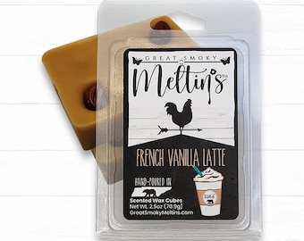 May include: A clear plastic package containing a brown wax melt cube with the text "GREAT SMOKY Meltin's" and "FRENCH VANILLA LATTE" on the label. The label also includes a hand-drawn illustration of a rooster and a cup of coffee. The wax melt is hand-poured and weighs 2.5 ounces (70.9 grams).