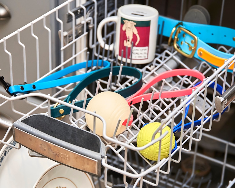 K&ouml;nnte beinhalten: Eine Sp&uuml;lmaschine mit verschiedenen Gegenst&auml;nden darin, darunter eine Tasse, ein Hundehalsband, ein Ball und ein Gummispielzeug. Die Gegenst&auml;nde sind in verschiedenen Farben, darunter blau, rosa, gelb und gr&uuml;n.