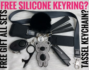 May include: A black and white rhinestone bear keychain with a black tassel, a black hand sanitizer holder, a black personal alarm, a black bottle opener, and a black lanyard with a black pom-pom.
