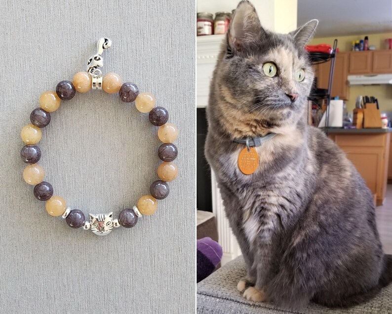 May include: A brown and grey beaded bracelet with a silver cat charm. The bracelet is made of natural stones and has a silver clasp.